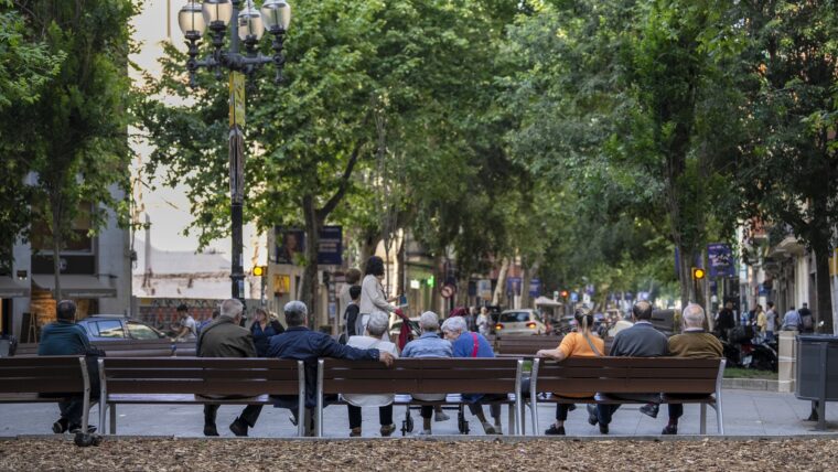 Un grup de persones grans assegudes en un banc a una plaça de la rambla del Poblenou.