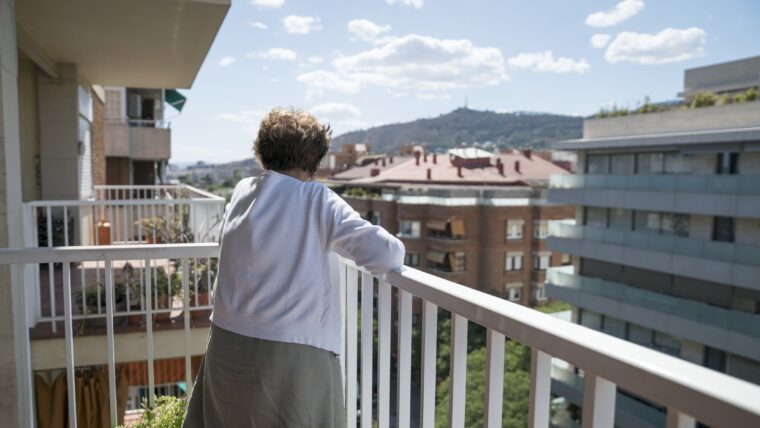 Una dona gran mira pel balcó de casa seva