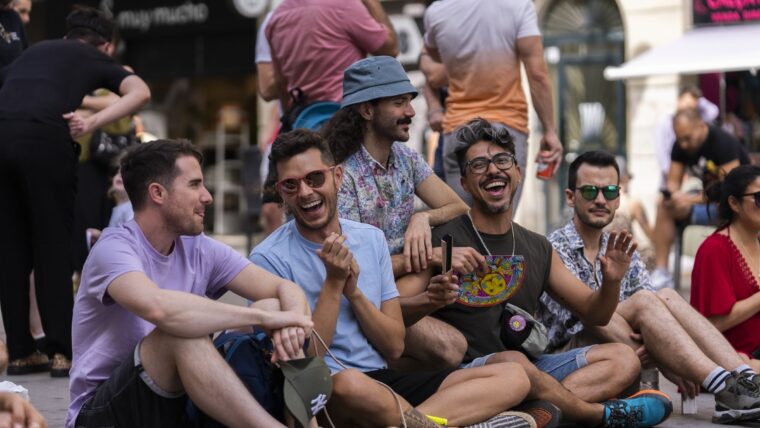 Grup de joves rient i conversant asseguts al terra a la Festa del Centre LGTBI de Barcelona 2022.