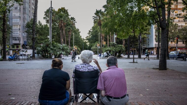 Una dona en cadira de rodes asseguda a la rambla de Prim acompanyada d'un home gran i d'una dona