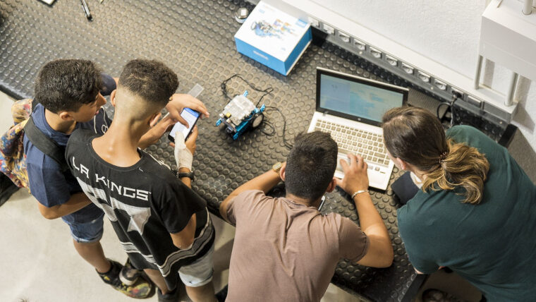 Grup de joves fent servir un ordinador per programar un robot.